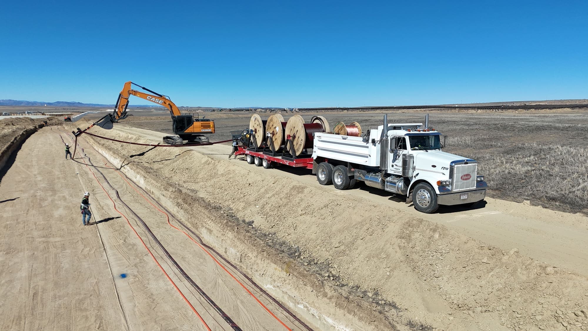 Excavator laying cable from a reel truck into a trench