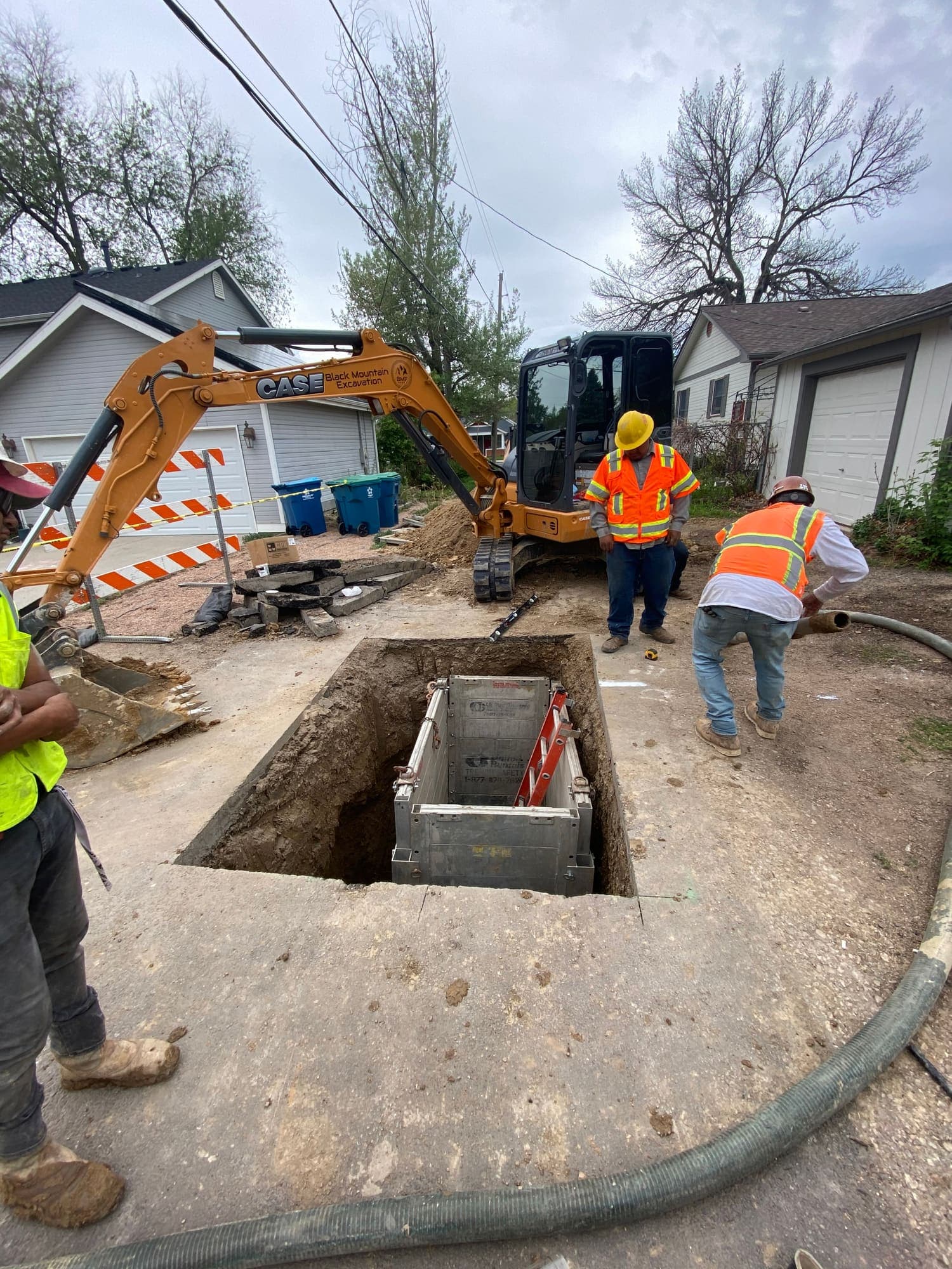 Crew setting a concrete vault in an alley excavation beside an excavator