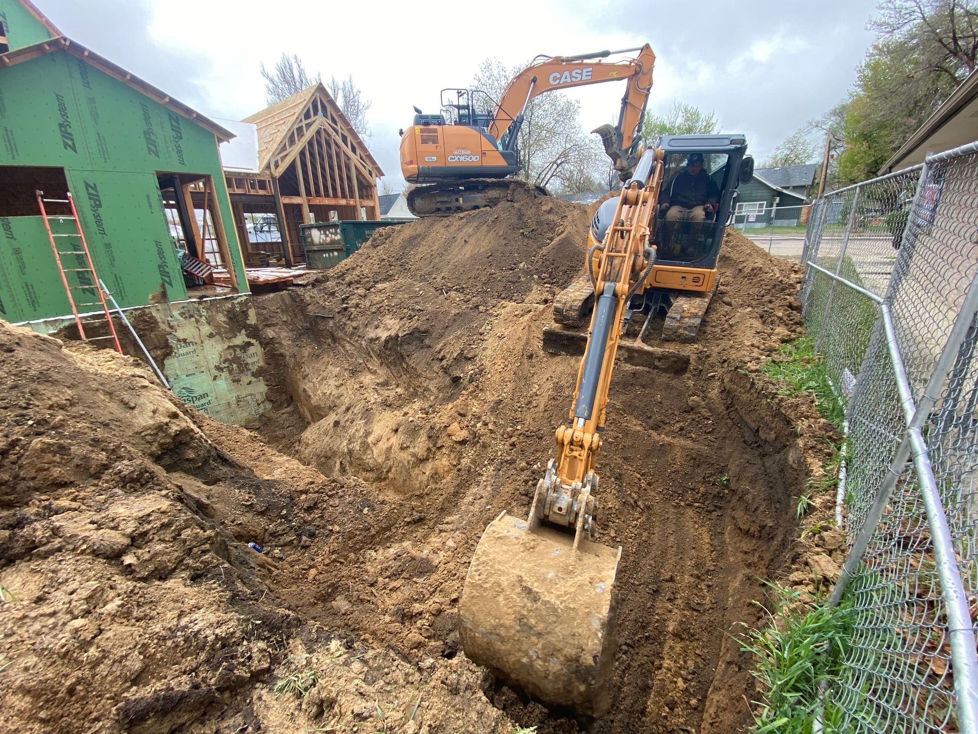 Excavator digging a deep trench next to a house under construction