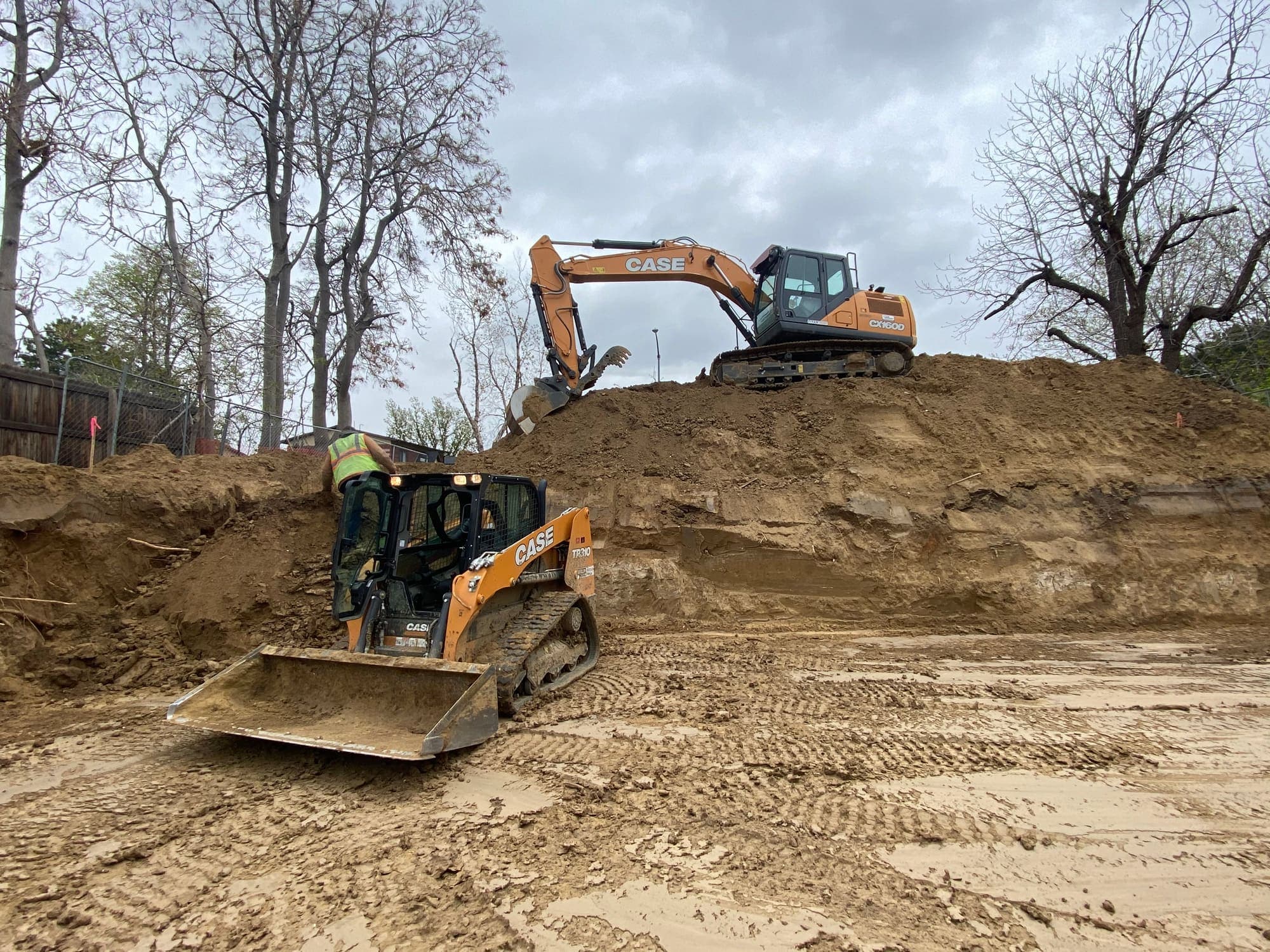 Track loader and excavator working a large dirt pile on a residential lot