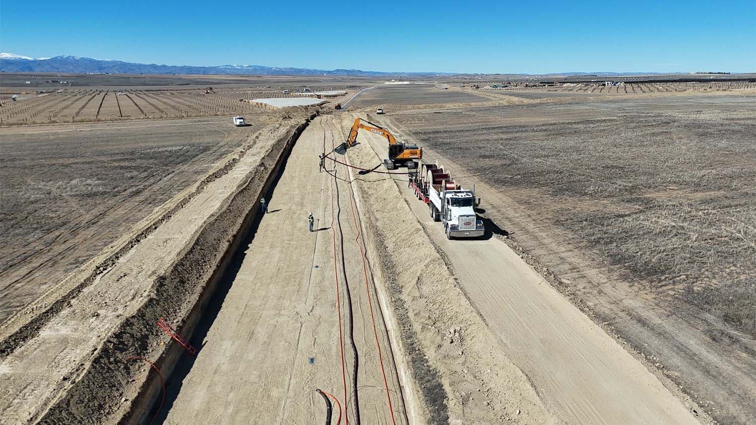 Drone view of an excavator and a cable-reel truck alongside a long open trench