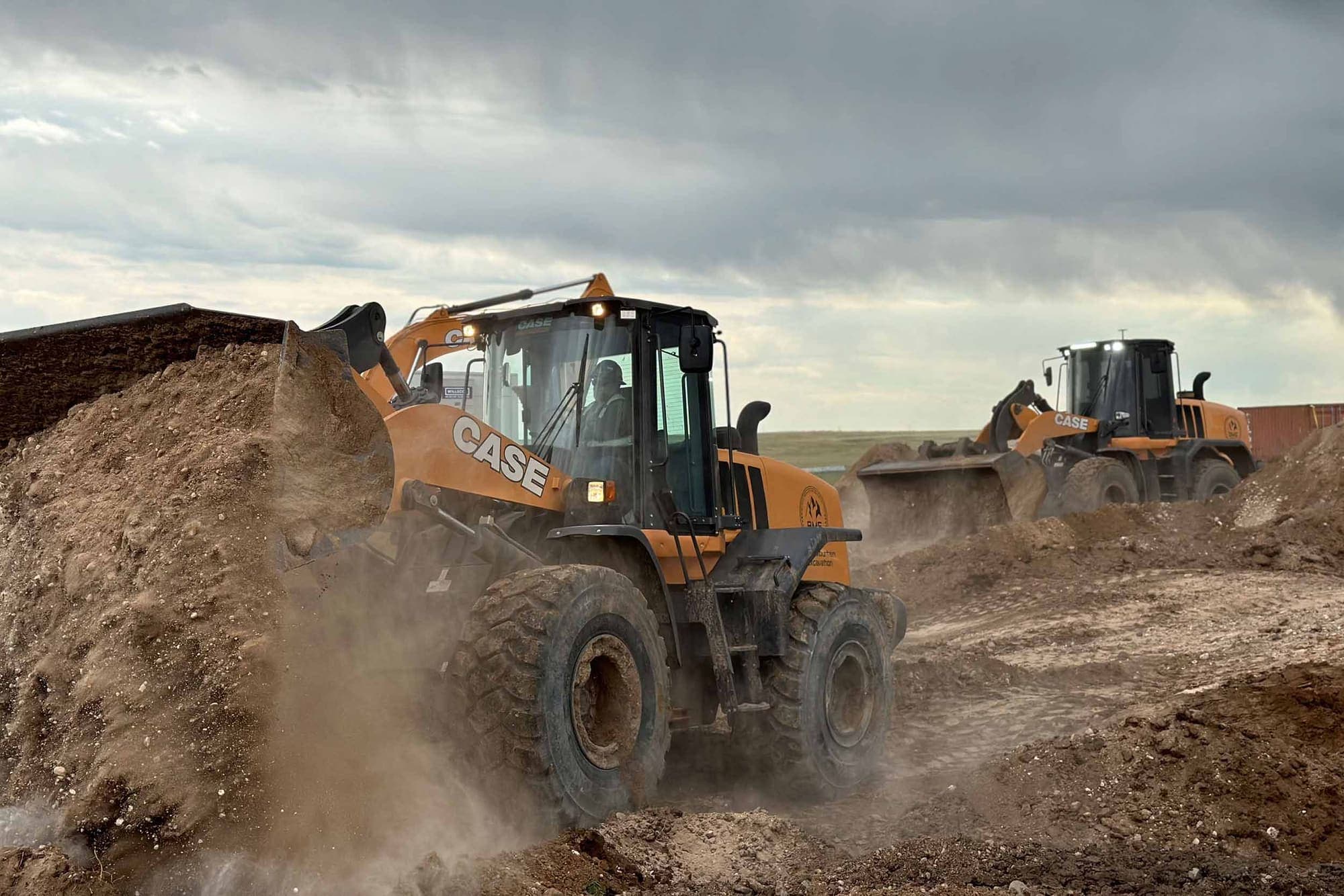 Two Case wheel loaders working dirt on a site under a cloudy sky
