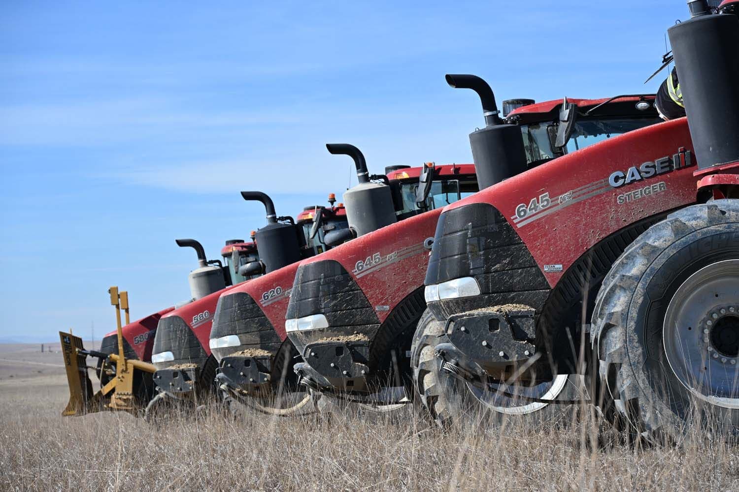 Row of red Case Quadtrac tractors with dozer blades parked on prairie grass
