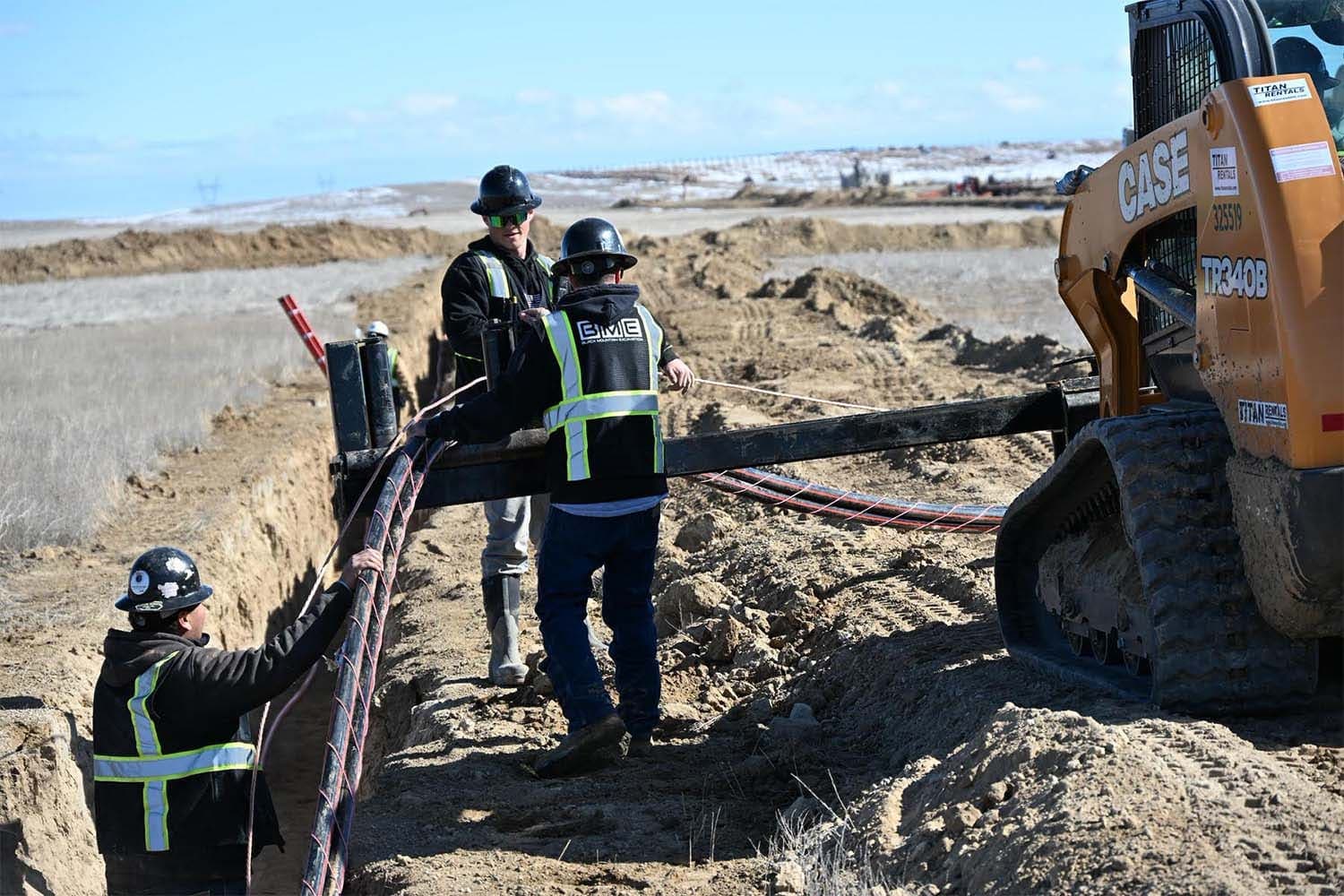 Crew feeding cable into a trench beside a tracked loader