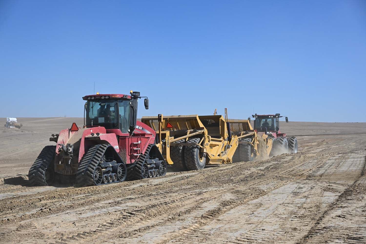 Red Case Quadtrac tractor pulling a yellow scraper across a graded site