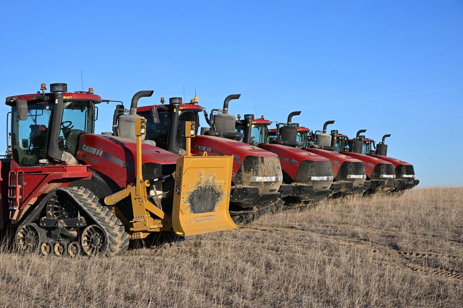 A row of red Case Quadtrac tractors parked side by side on prairie grass