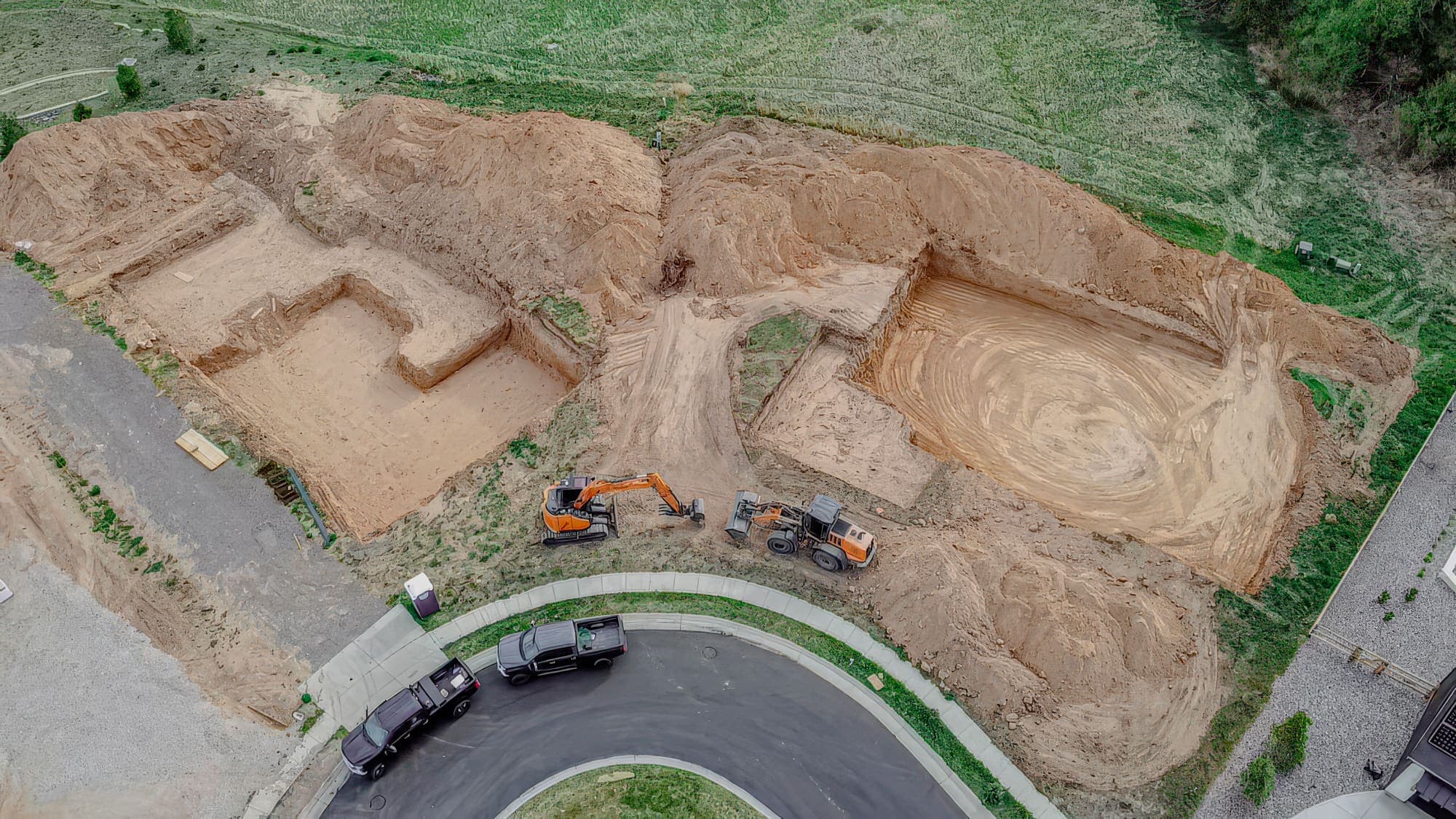 Aerial view of a residential lot dug out for foundations next to a curved street