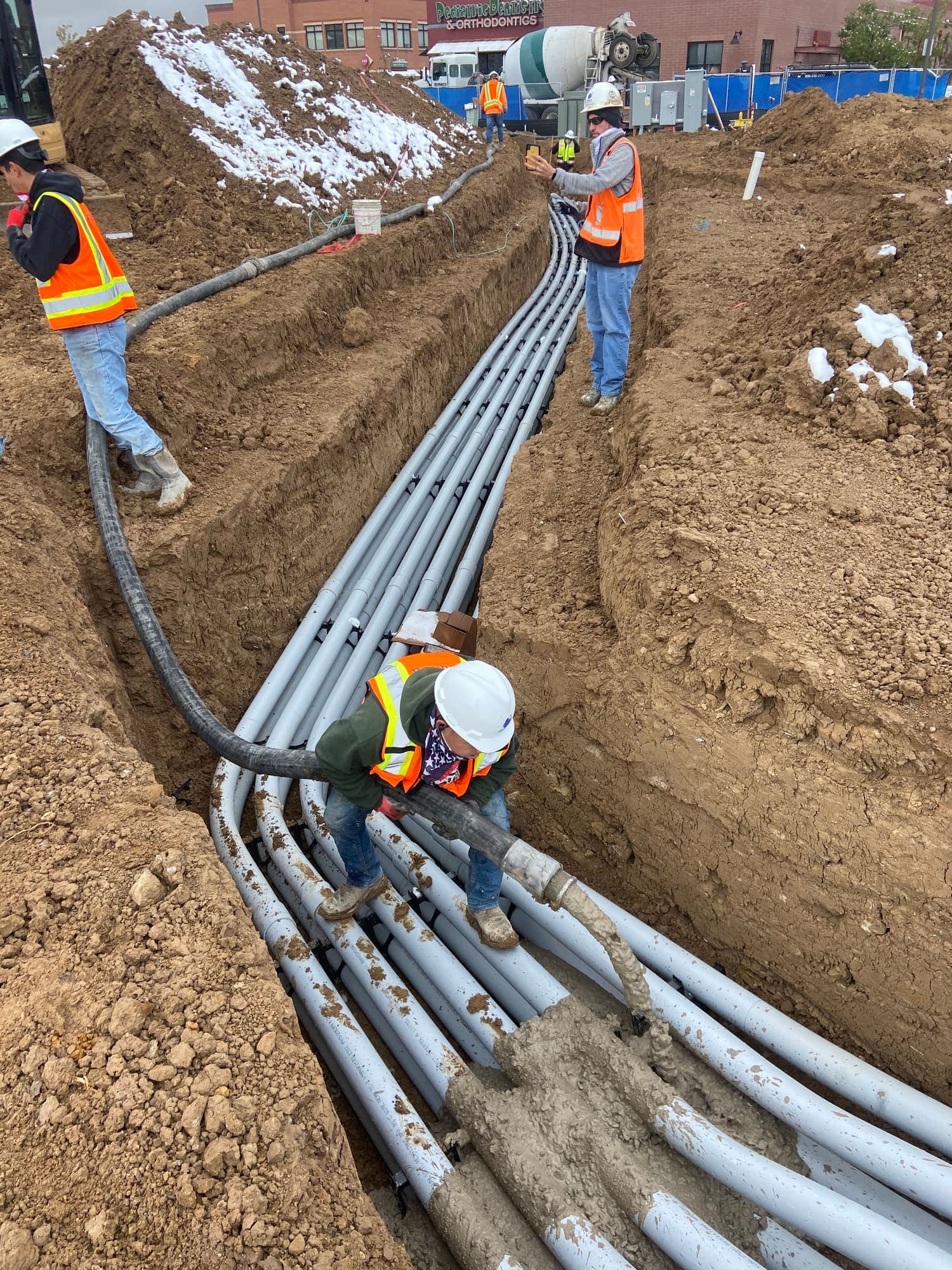 Worker in a trench guiding bundled gray electrical conduit