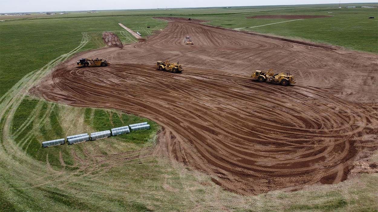 Aerial view of scrapers working a large graded pad cut into green prairie