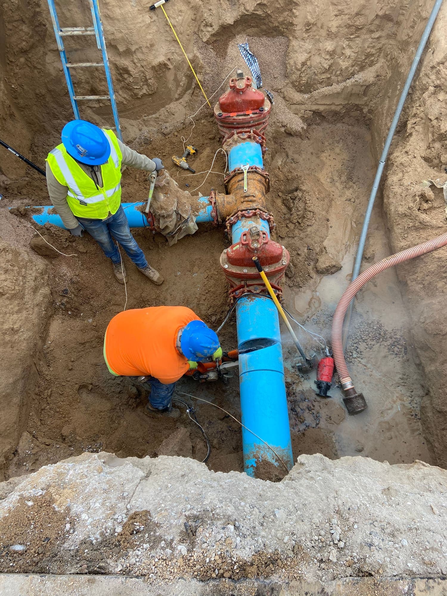 Crew installing a blue water main with a red valve in a trench
