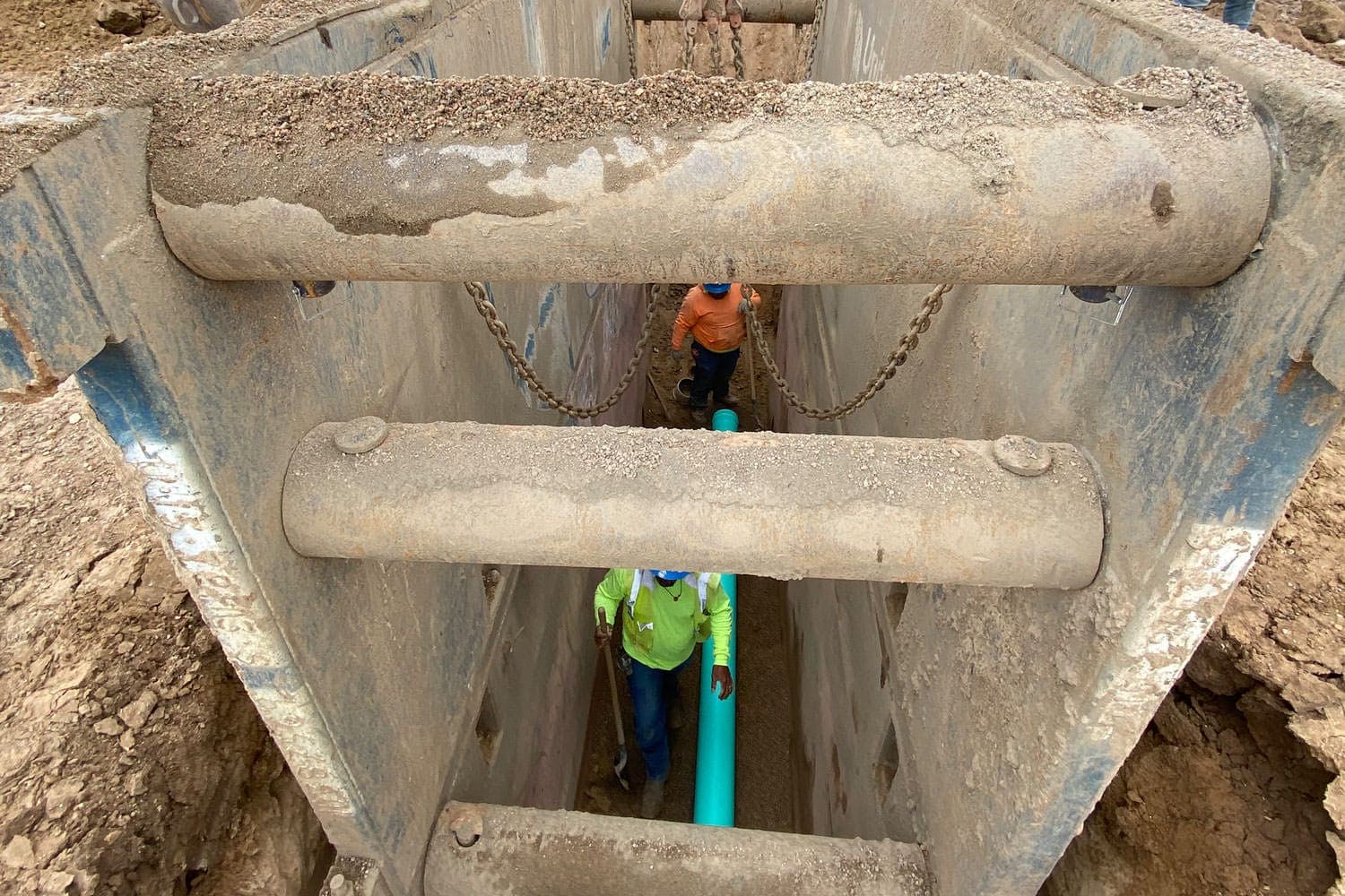Looking down into a shored trench at a worker laying blue pipe
