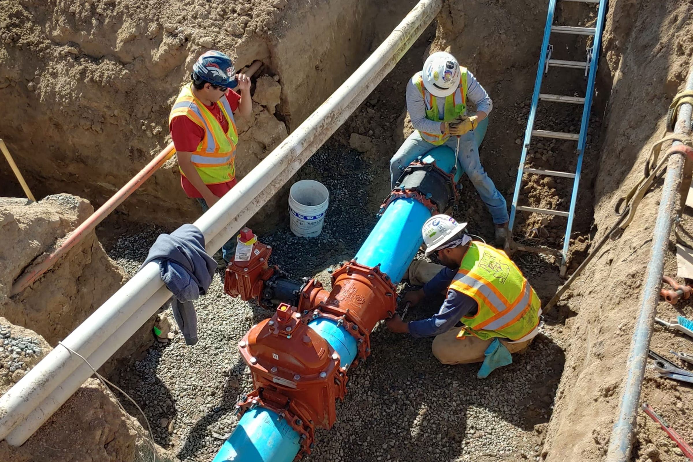 Crew working in a trench, fitting a red valve onto a blue water main